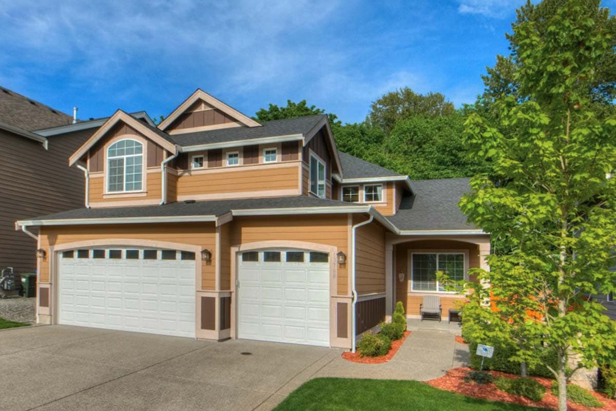 House plan exterior. Two-story home with a gabled roof, two-car garage, and dormers. Features include a front porch and multi-pane arched windows.