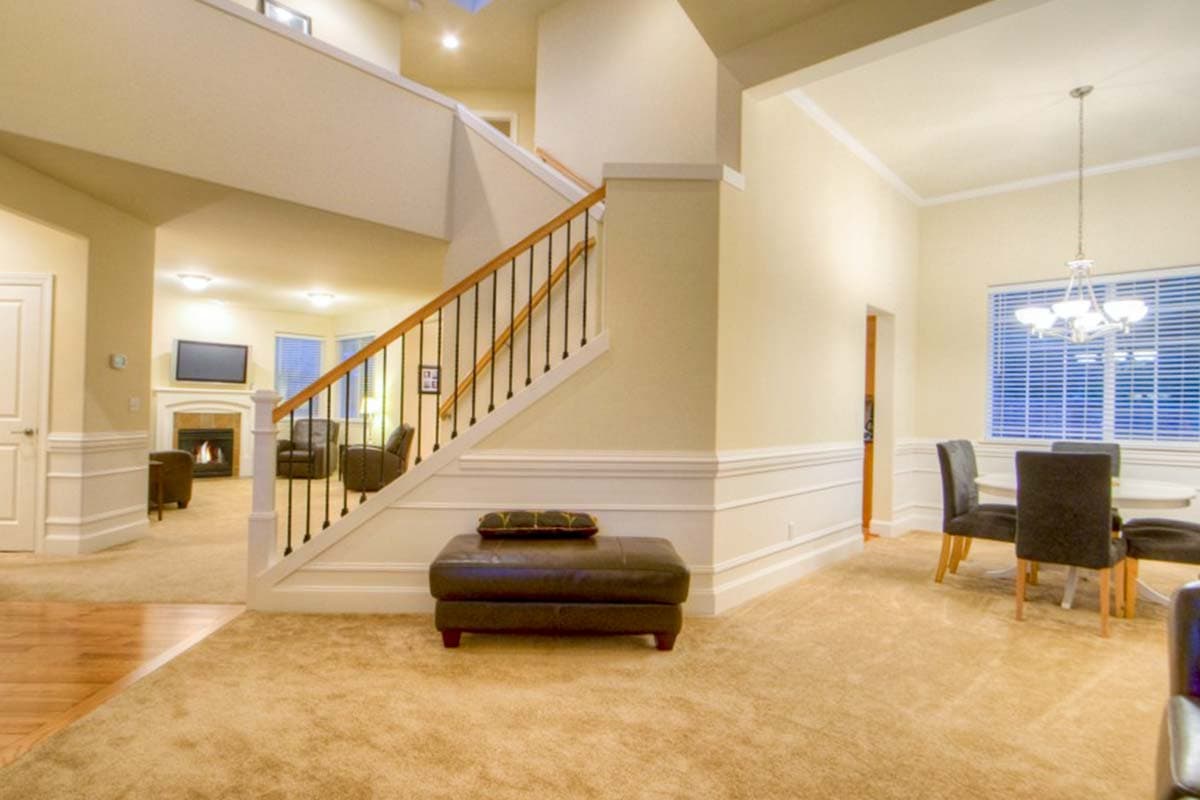 Interior view of open concept living area with fireplace, grand staircase, and dining room with chandelier.