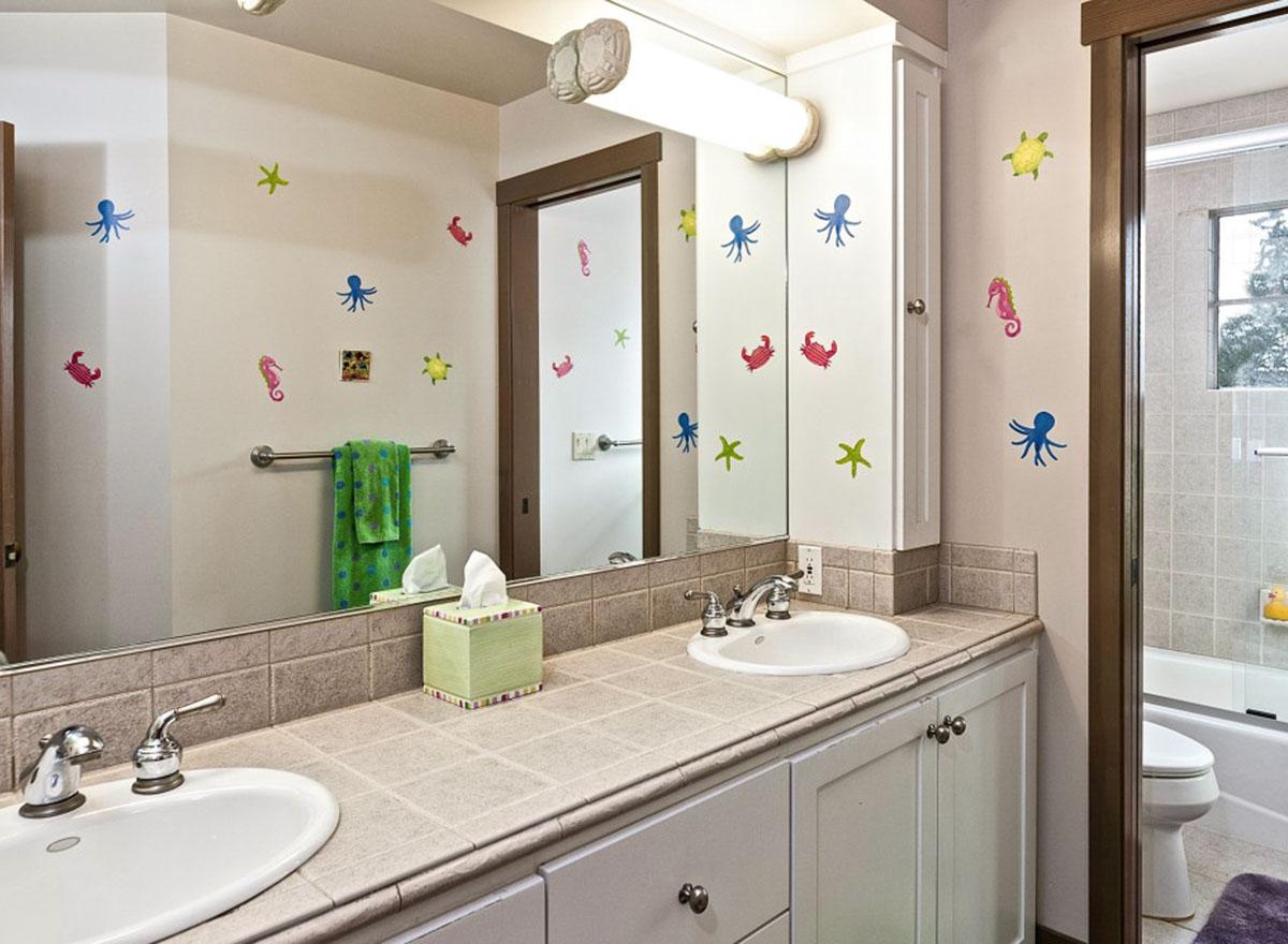 Bathroom with double vanity, tiled countertop, and sea creature wall decals. Tub/shower visible.
