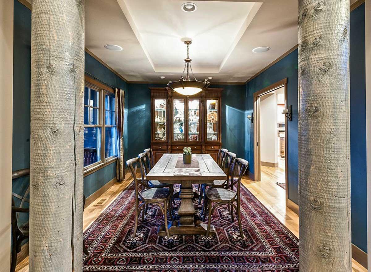 Dining room with beamed ceiling, paneled walls, wooden table, chairs, hutch, and ornate rug.