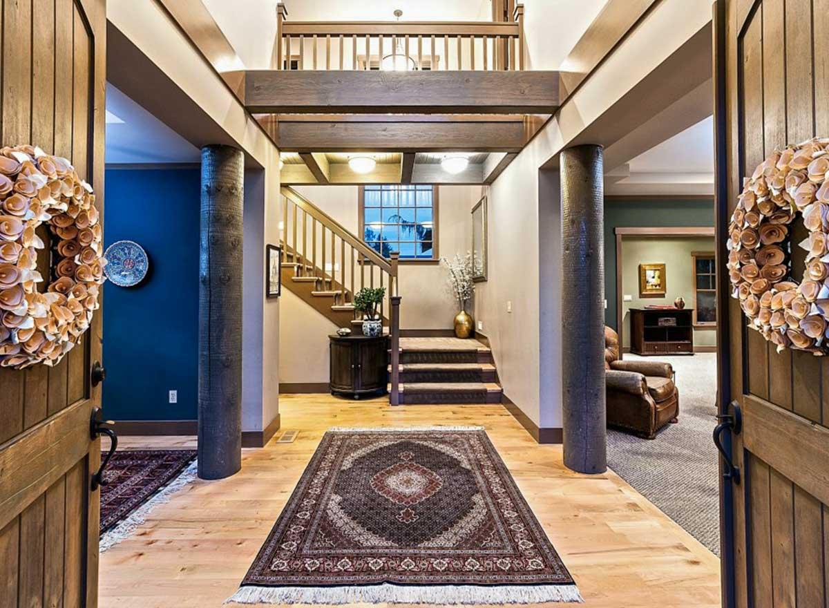 Interior entry foyer with wood beams, stone-clad columns, staircase, and upper-level balcony.