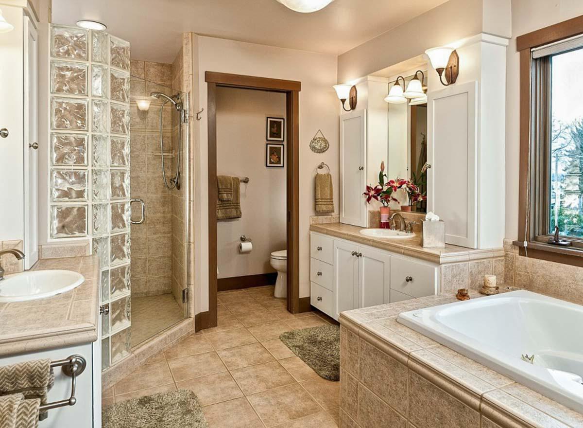 Bathroom interior with glass block shower, dual vanity with white cabinets, soaking tub, and separate toilet area.