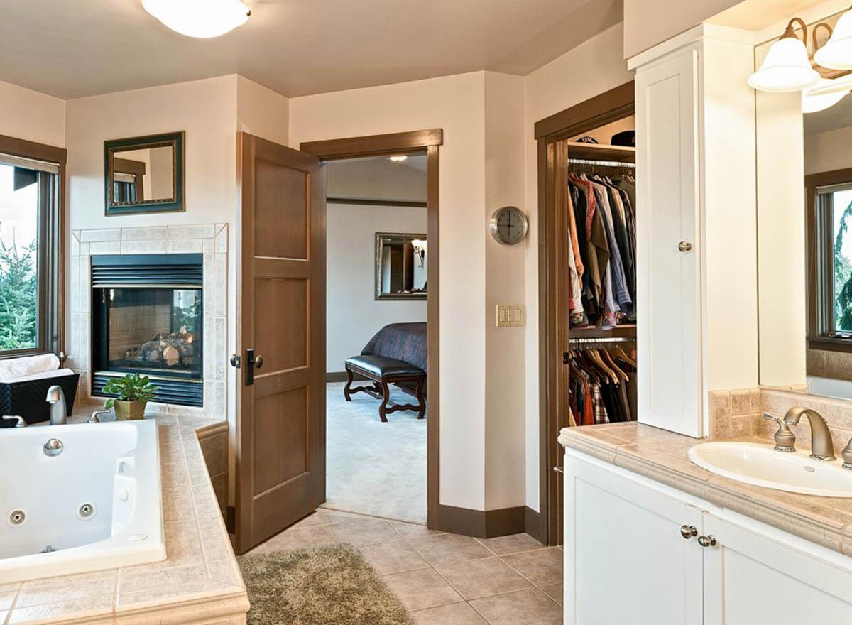 Bathroom with whirlpool tub, fireplace, walk-in closet, and view of bedroom with bench.