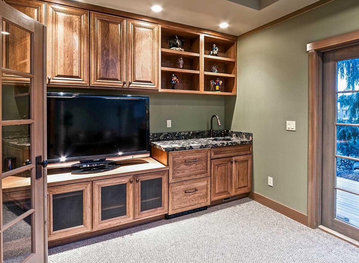 Interior view of a media room featuring wood cabinetry, a wet bar with granite countertop, and a television.