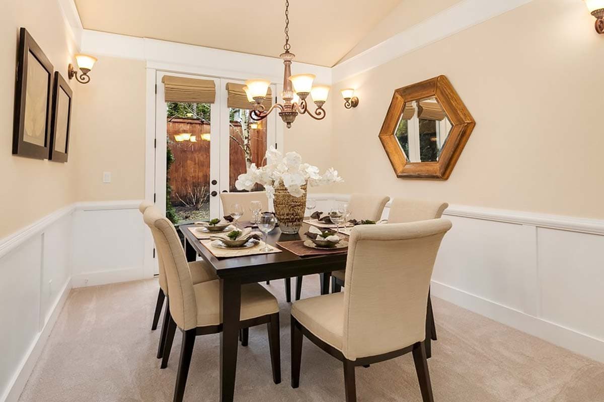 Dining room with vaulted ceiling, wainscoting, chandelier, and French doors leading outside.
