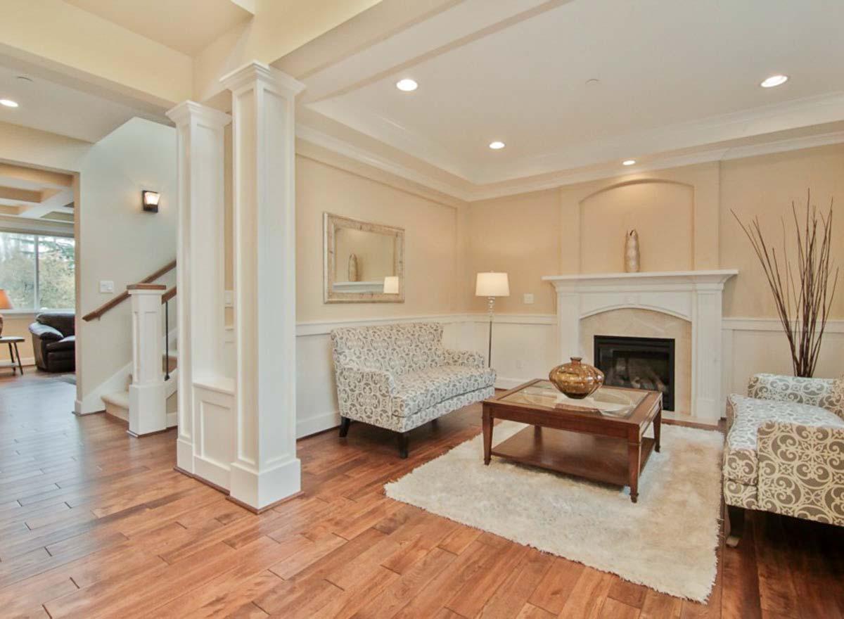 Living room with fireplace, coffered ceiling, and wood floors. Staircase visible in background.