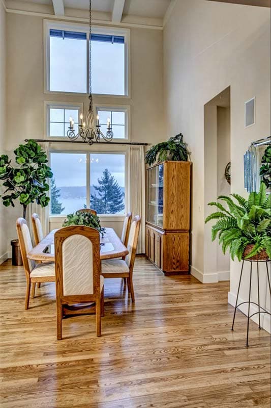 Dining room with vaulted ceiling, large windows, wooden dining table and chairs, and a built-in cabinet.
