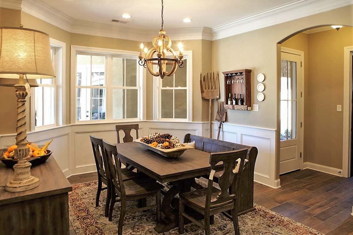 Dining room with wooden table and chairs, bay windows, wainscoting, and a rustic wine rack.