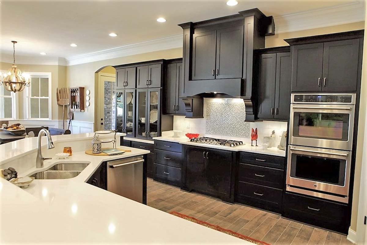 Kitchen with dark cabinets, large island with sink, built-in ovens, and gas range with decorative backsplash.