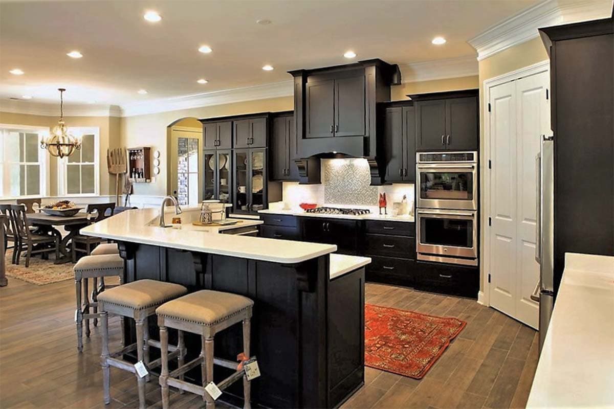 Contemporary kitchen with dark cabinetry, double ovens, island with seating, and adjacent dining area.
