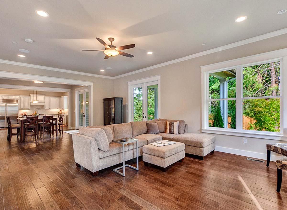 Open concept living area with large sectional, view of dining and kitchen, and large windows.