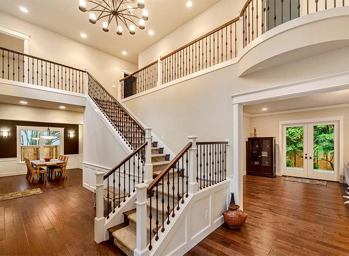 Interior view of house entryway with double staircase, grand chandelier, open loft, and dining area.