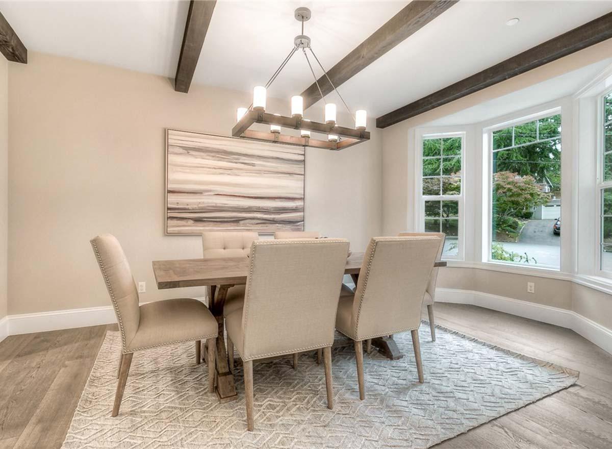 Dining room with wood-beamed ceiling, bay window, and a rustic wood table with upholstered chairs.
