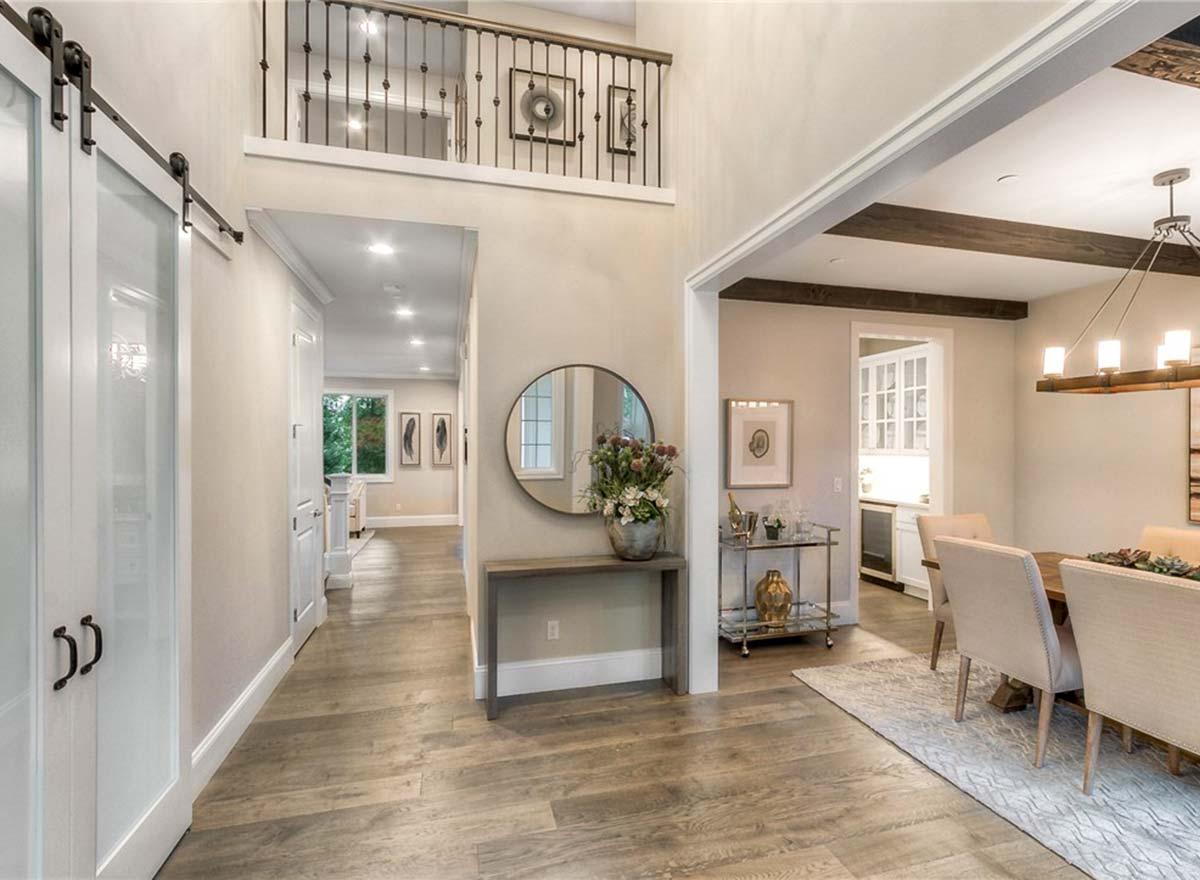 Interior view of hallway with barn door, second-story railing, round mirror and dining room.