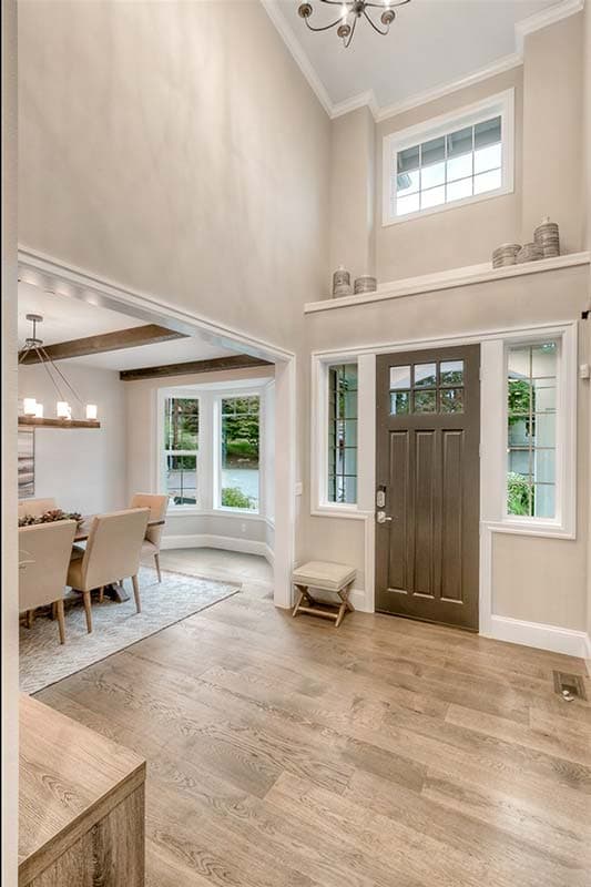 Interior view: Foyer with double-height ceiling, dark paneled door with glass panes, and view into dining room with beamed ceiling.
