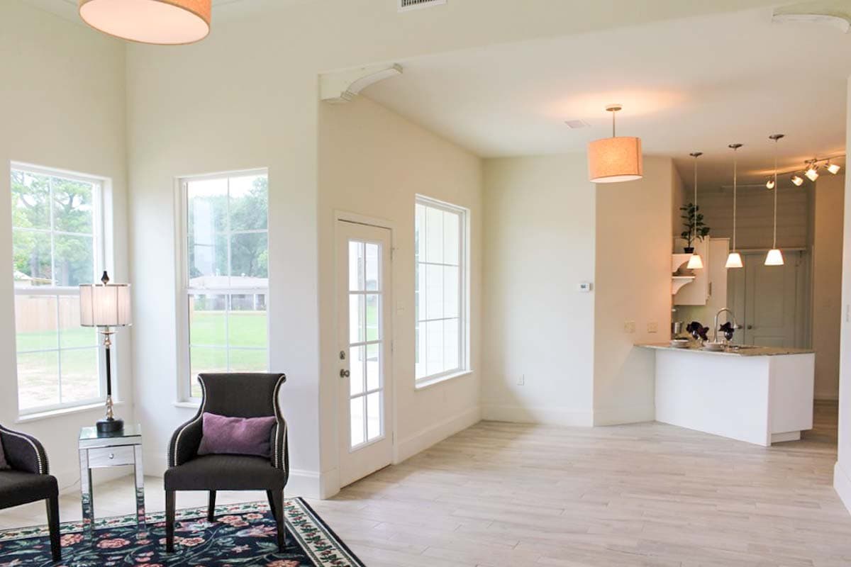 Interior view of a house plan showing a living area with large windows, a kitchen island, and pendant lighting.
