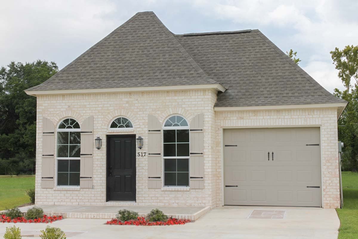 House plan exterior. One-story brick home with arched windows, shutters, a gable roof, and an attached garage.
