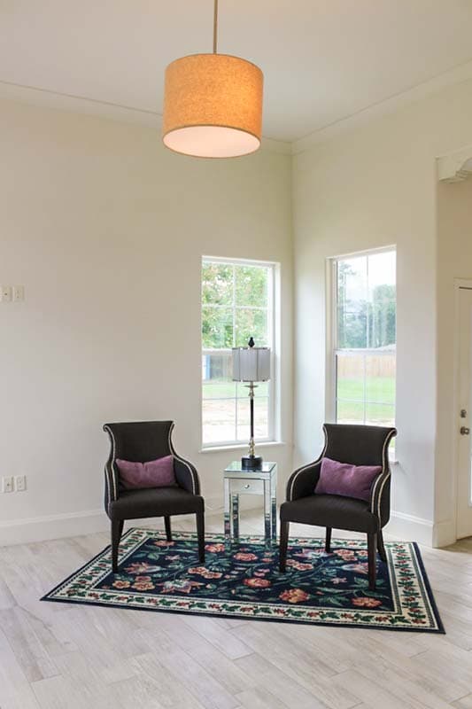 Interior view of a seating area with two upholstered chairs, a floral rug, and two windows.