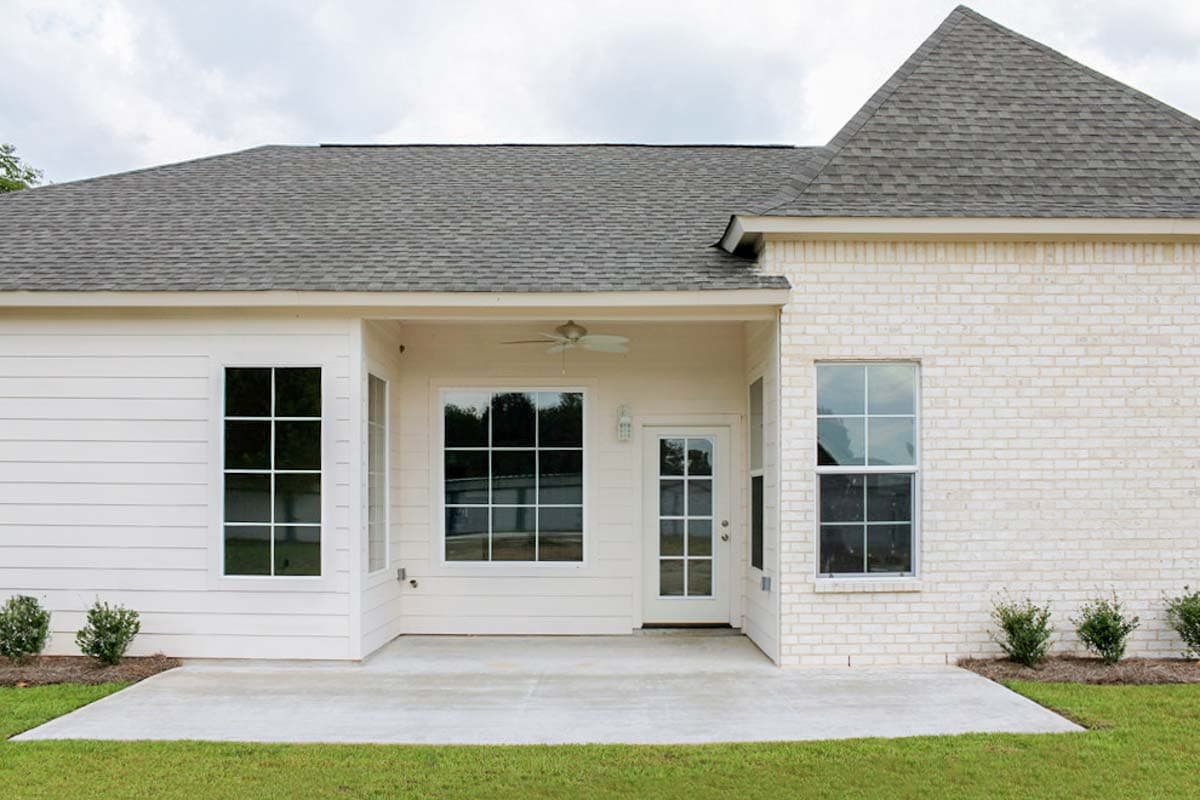 House plan exterior with white brick and siding, covered patio with ceiling fan, and multiple large windows.