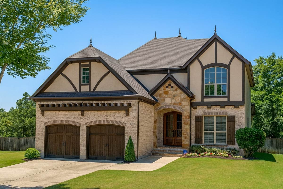 House plan exterior. Two-story Tudor style home with gables, stone accents, and a two-car garage. Features arched doorways and window trim.