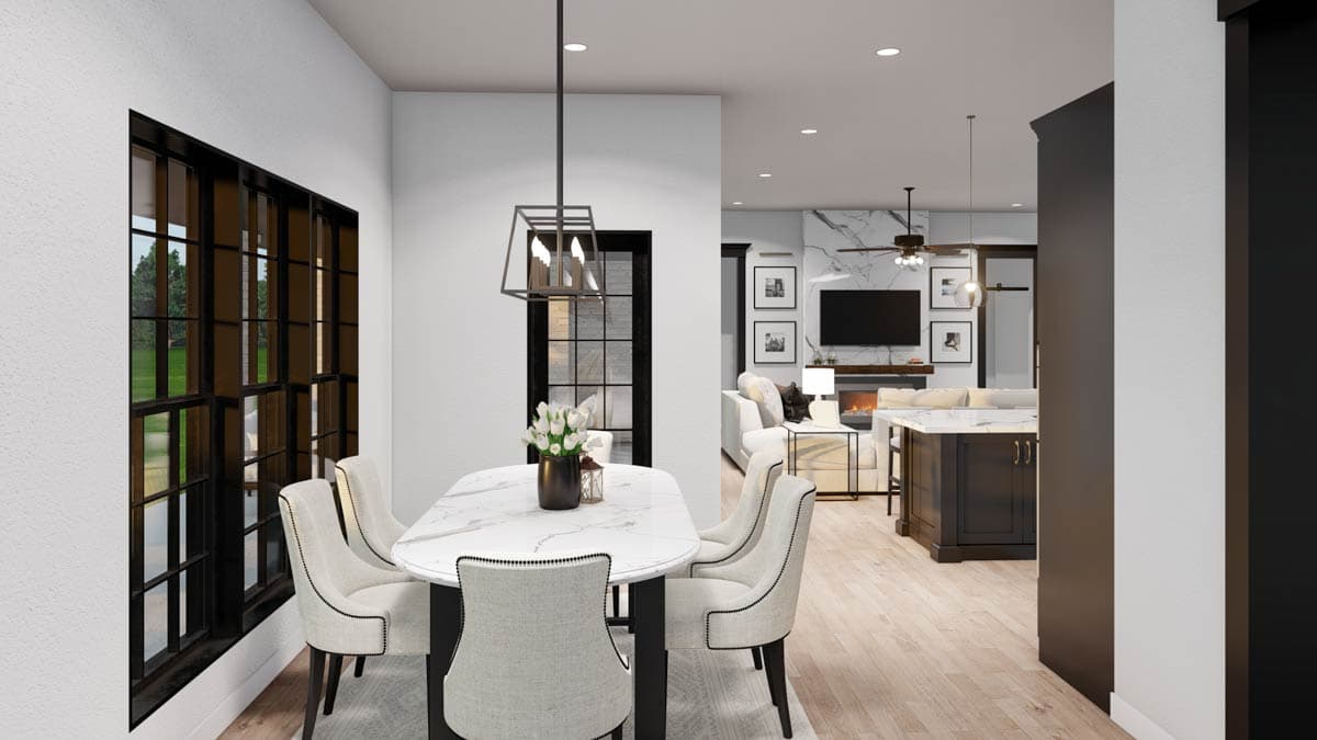 Dining area with large grid windows and chairs, opening to great room with fireplace, TV, and kitchen island.