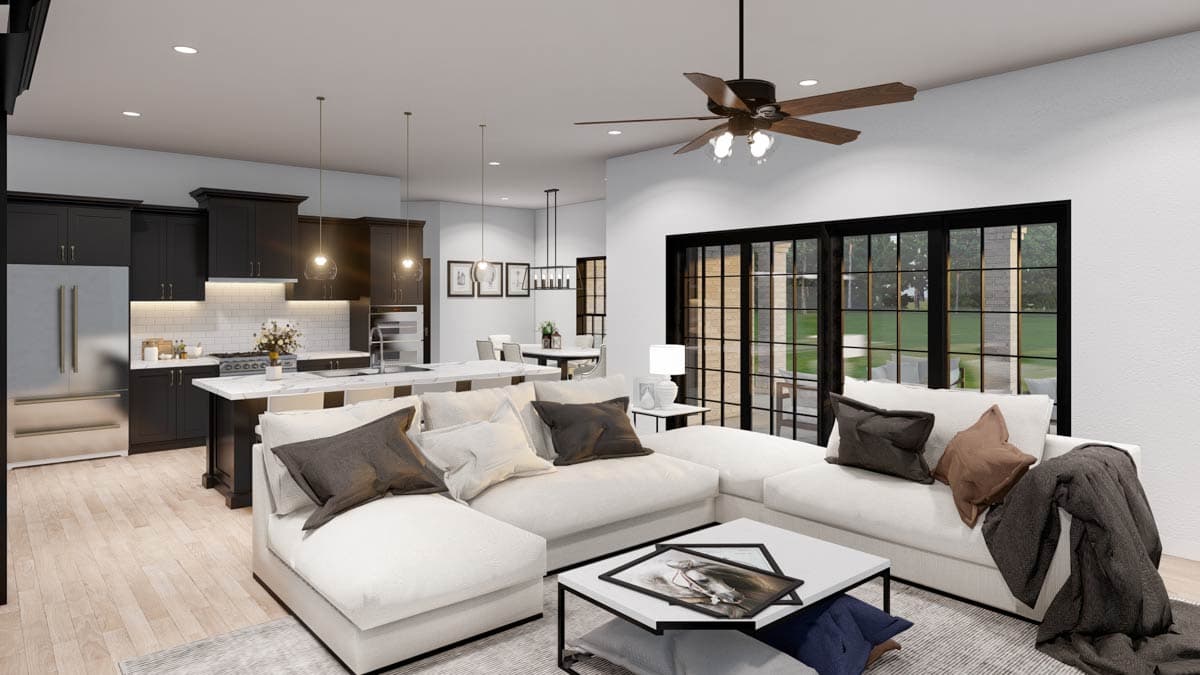 Open concept living area with a kitchen island, sectional sofa, and large windows overlooking a yard.