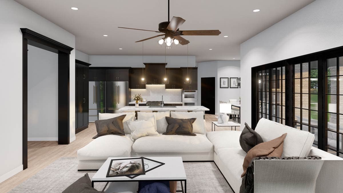 Open concept living space with sectional sofa, kitchen island, and modern dark cabinetry. Large windows overlook outdoor area.