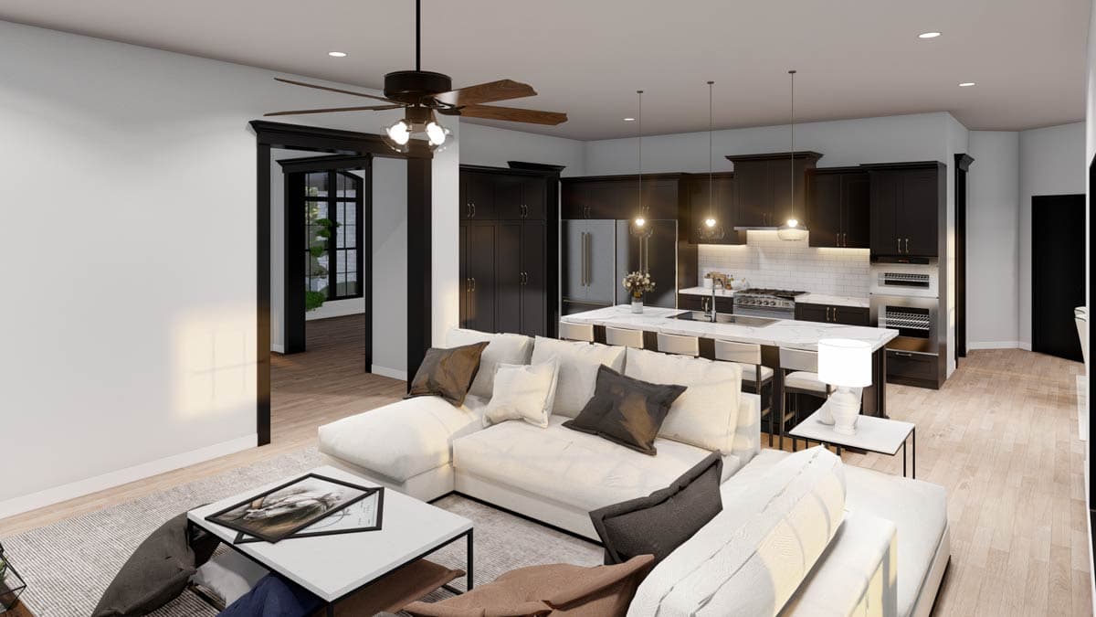 Open-concept living area with sectional sofa, kitchen island, and dark cabinetry. Leads to a doorway with a large window.