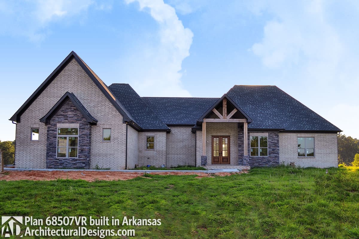 House plan exterior: Single-story brick home with stone accents, a covered front porch with timber details, and multiple gables.