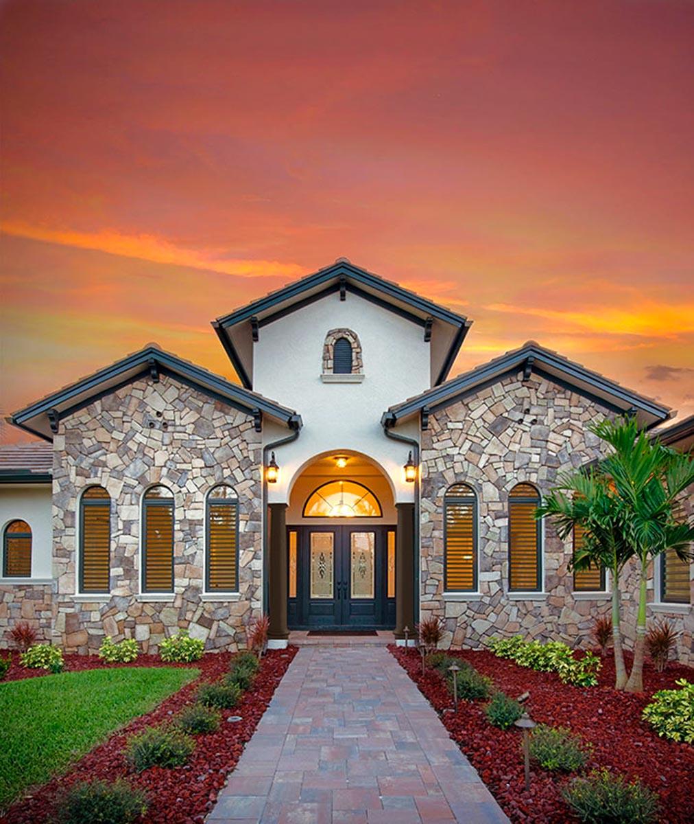 House plan exterior: Stone facade, arched windows, double entry doors, covered archway, gabled roofs.