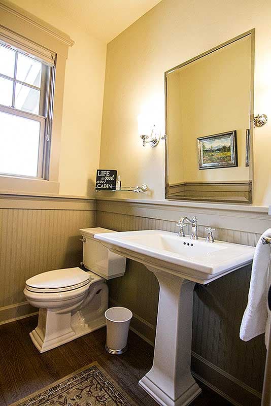 Bathroom with pedestal sink, toilet, wainscoting, and a mirrored medicine cabinet.