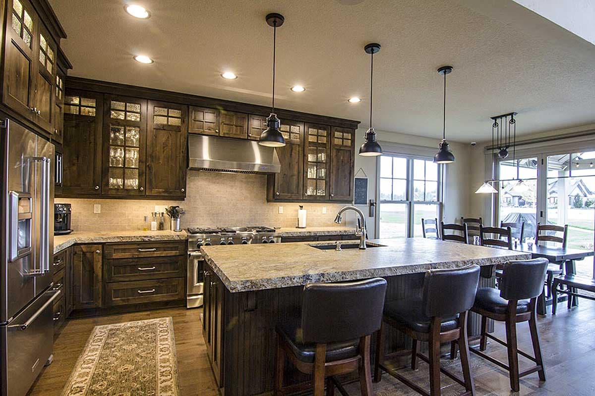 Kitchen with dark wood cabinetry, granite island with seating, stainless steel appliances, and dining area with large windows.