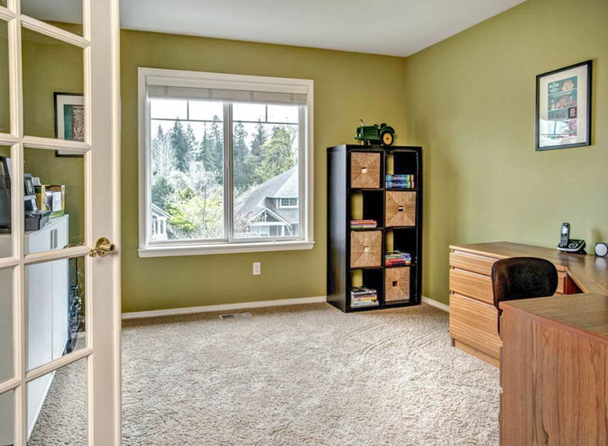 Office with desk, shelving unit, and French door. Window overlooks wooded area and house exterior.