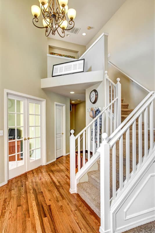 Interior view of entryway with double glass doors, hardwood floors, and a carpeted staircase with white banister.