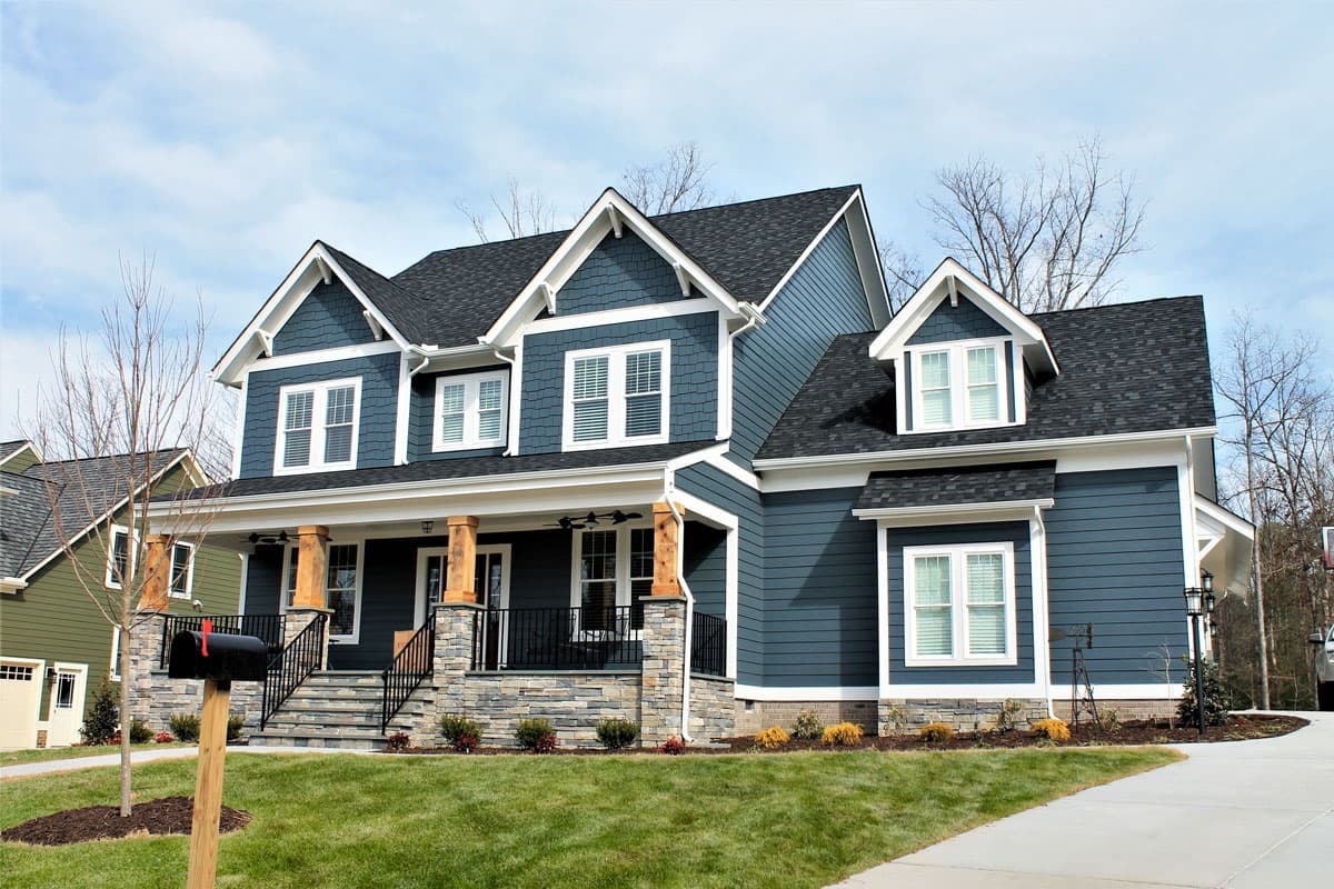 Two-story Modern Farmhouse exterior with wide front porch, stone base, multiple gables, and dormer windows.