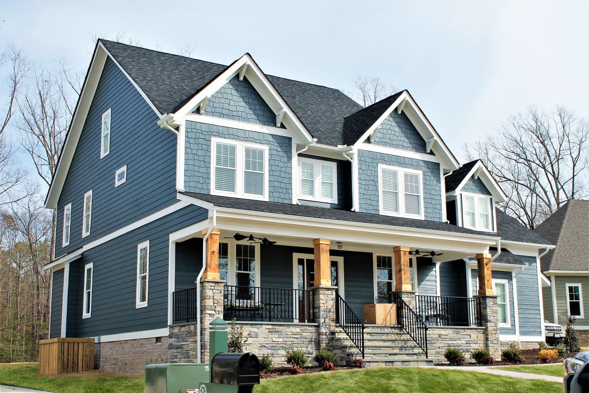 House plan exterior of a two-story home with blue siding, stone accents, large covered porch, and multiple gables.