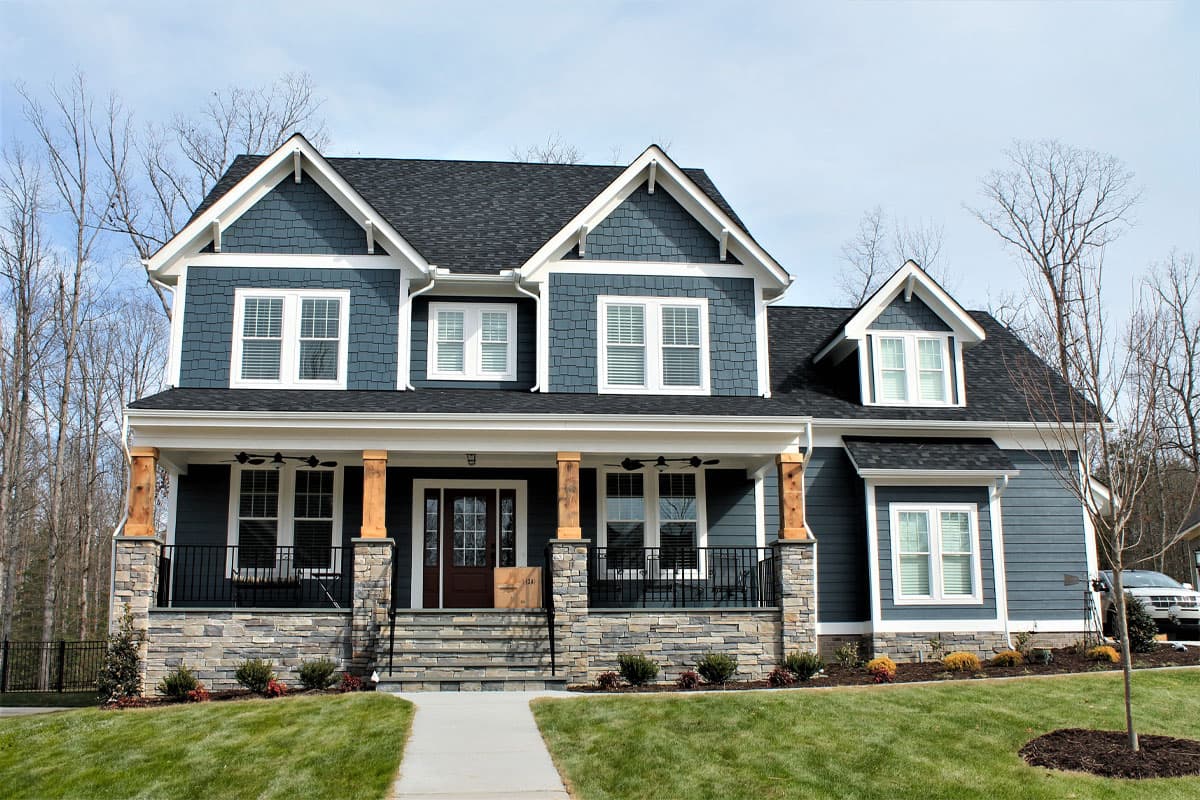 Craftsman-style two-story house plan exterior. Features include a front porch with stone and wood columns, multiple gables, and a dark shingle roof.