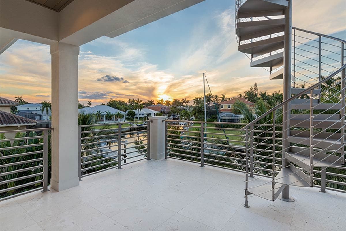 House plan exterior with a covered balcony featuring a spiral staircase and waterfront views at sunset.