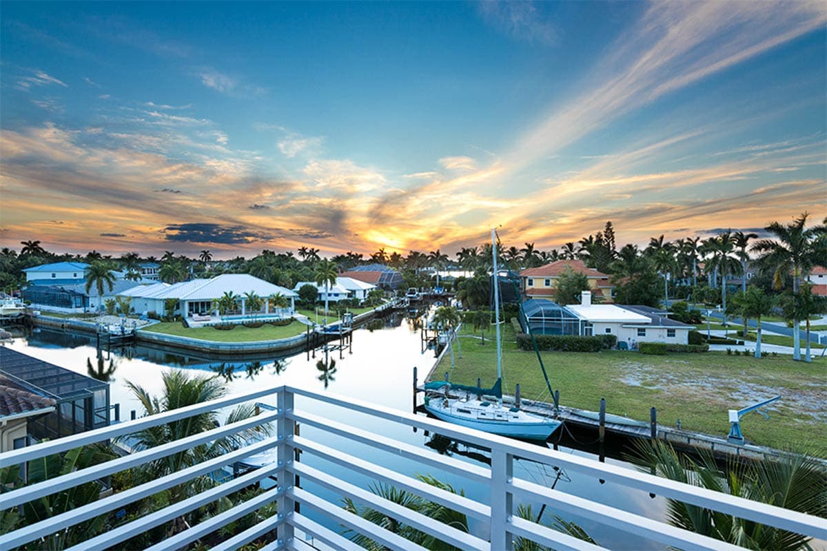 House plan exterior with canal, docks, and boat. Single-story homes with varied rooflines and tropical landscaping.