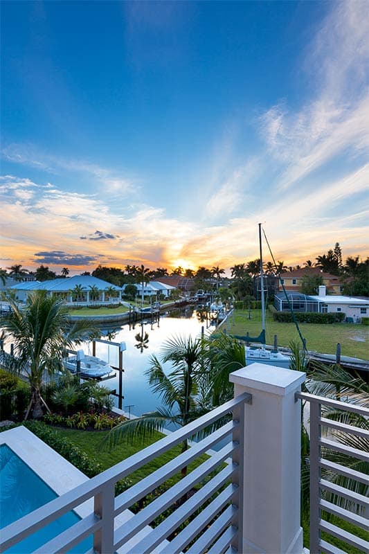 Waterfront property with canal, docks, boats, palm trees, and houses under a sunset sky.