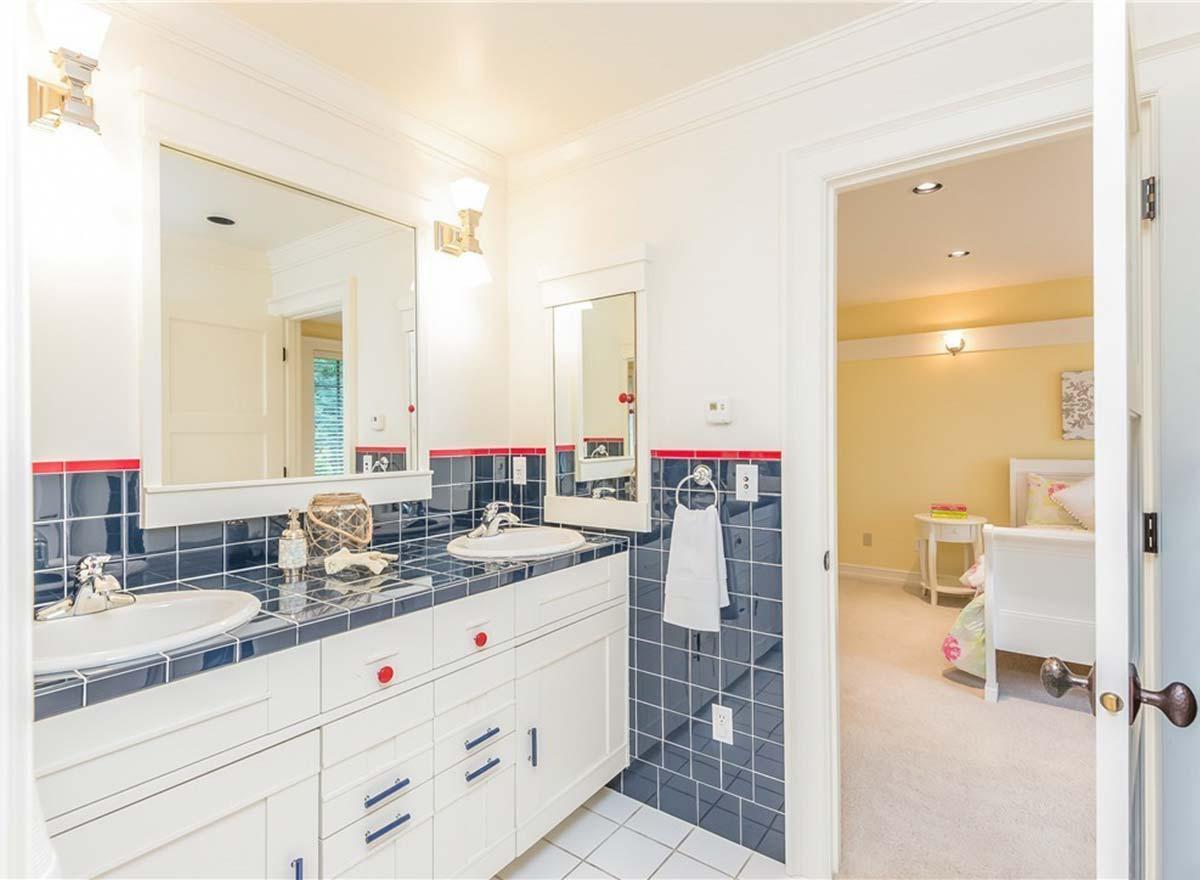 Bathroom with double vanity, navy tile backsplash with red trim, and view into a yellow bedroom.