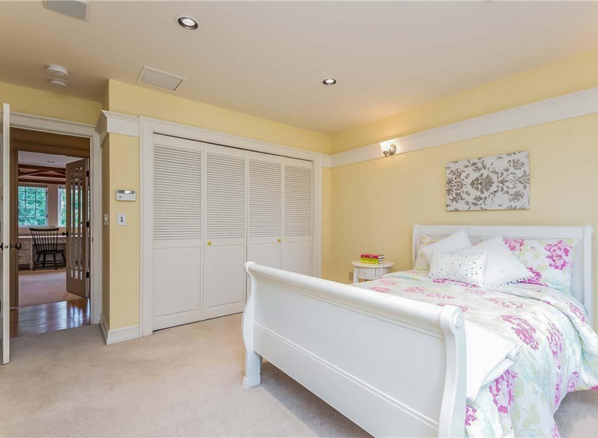 Bedroom interior with white sleigh bed, louvered closet doors, and doorway to an adjacent office or den.