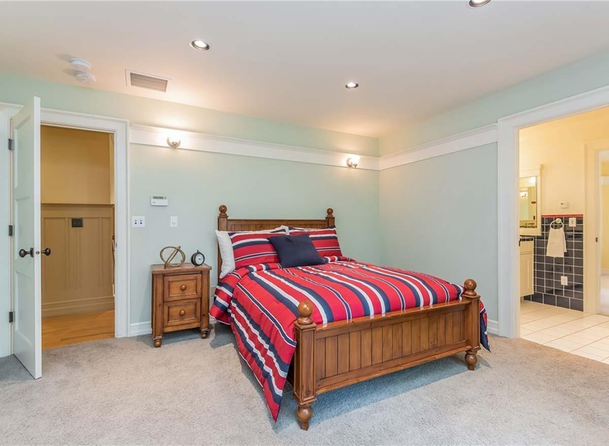 Bedroom with wooden bed, striped bedding, and nightstand. Door opens to wood-paneled hallway. Adjacent bathroom visible.