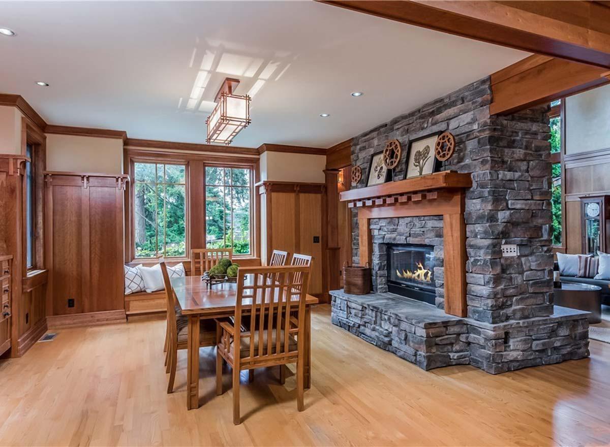 Dining area with wood table and chairs, stone fireplace, built-in window seat, and large windows.