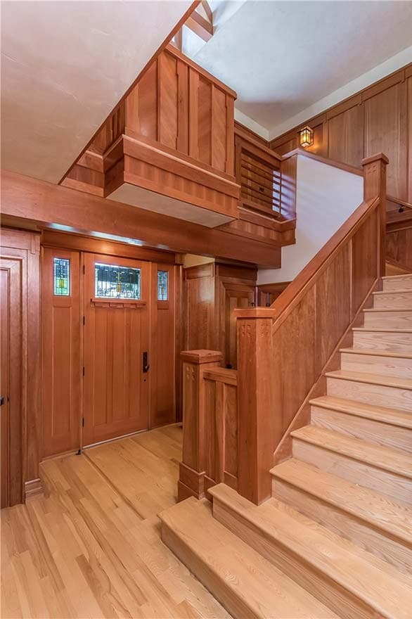 Interior view of a Craftsman-style entryway with wood paneling, stained glass window door, and wooden staircase.