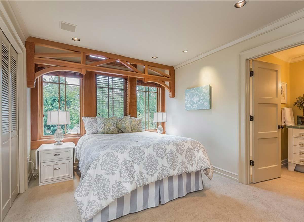 Bedroom with wooden window trim, central bed, and open doorway to an en suite bathroom.