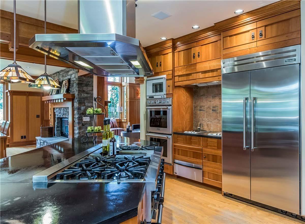 Kitchen with island cooktop, stone fireplace, stainless steel appliances, and wood cabinetry.