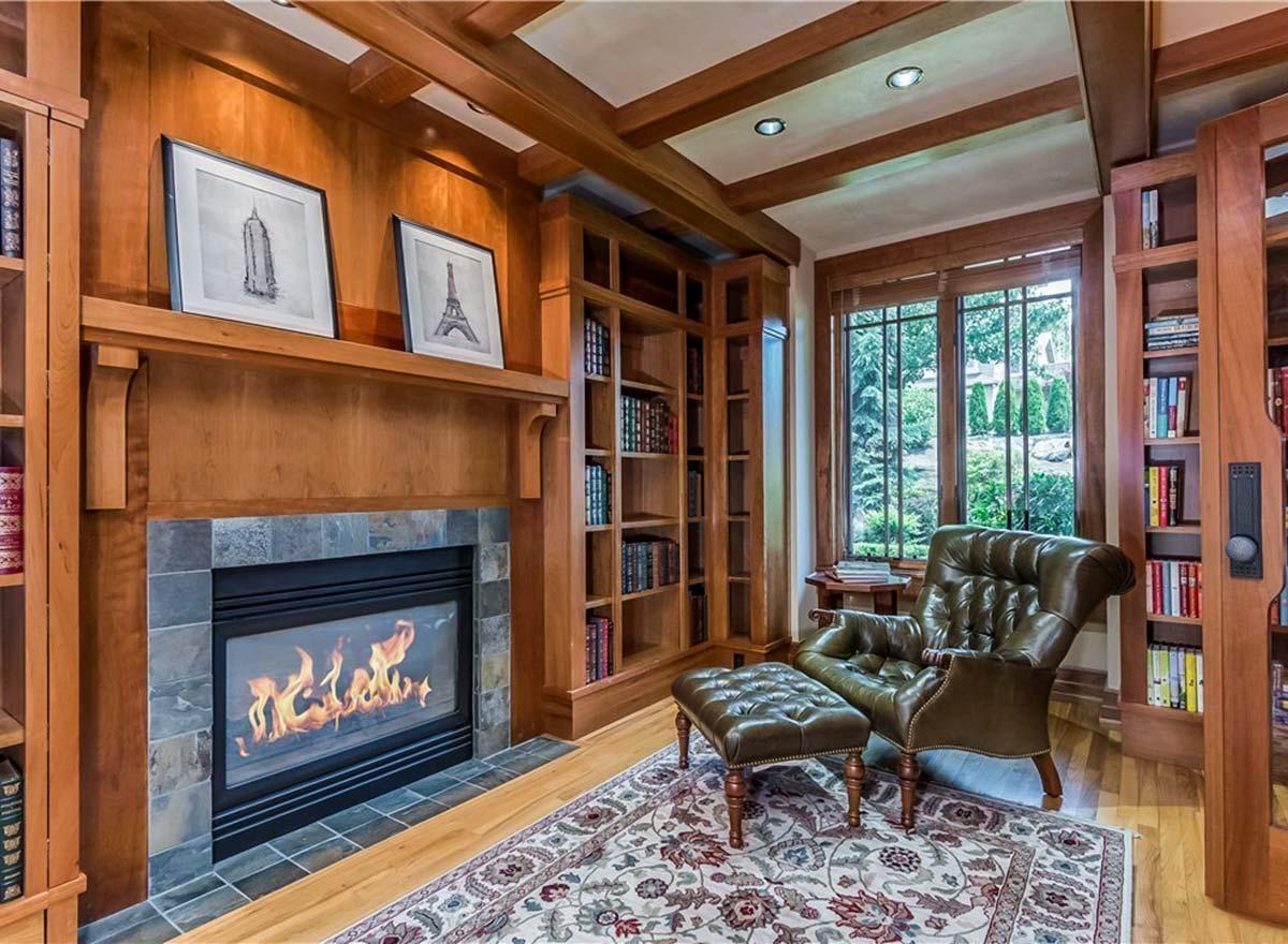 Library with built-in wood bookshelves, fireplace with stone surround, and tufted leather armchair with ottoman.