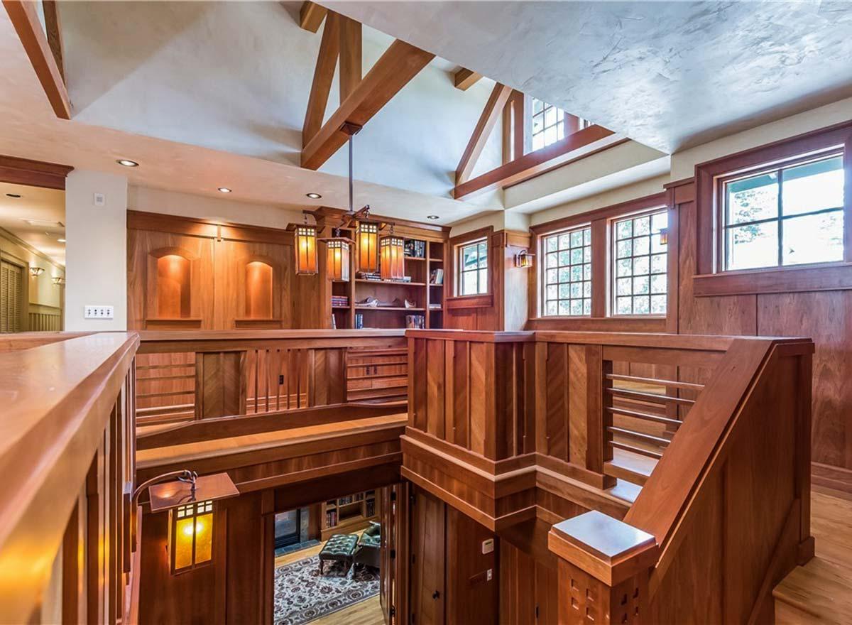 Interior view of a wood-paneled hallway with exposed beams, built-in bookshelves, and a multi-tiered chandelier.