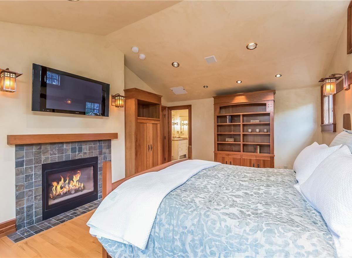 Bedroom with fireplace, built-in bookshelves, and television. Doorway to ensuite bathroom visible.
